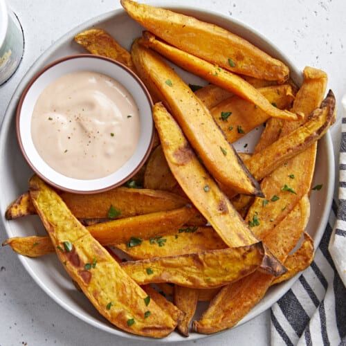 Overhead view of a plate of sweet potato fries served with mayo ketchup dipping sauce and a napkin on the side.