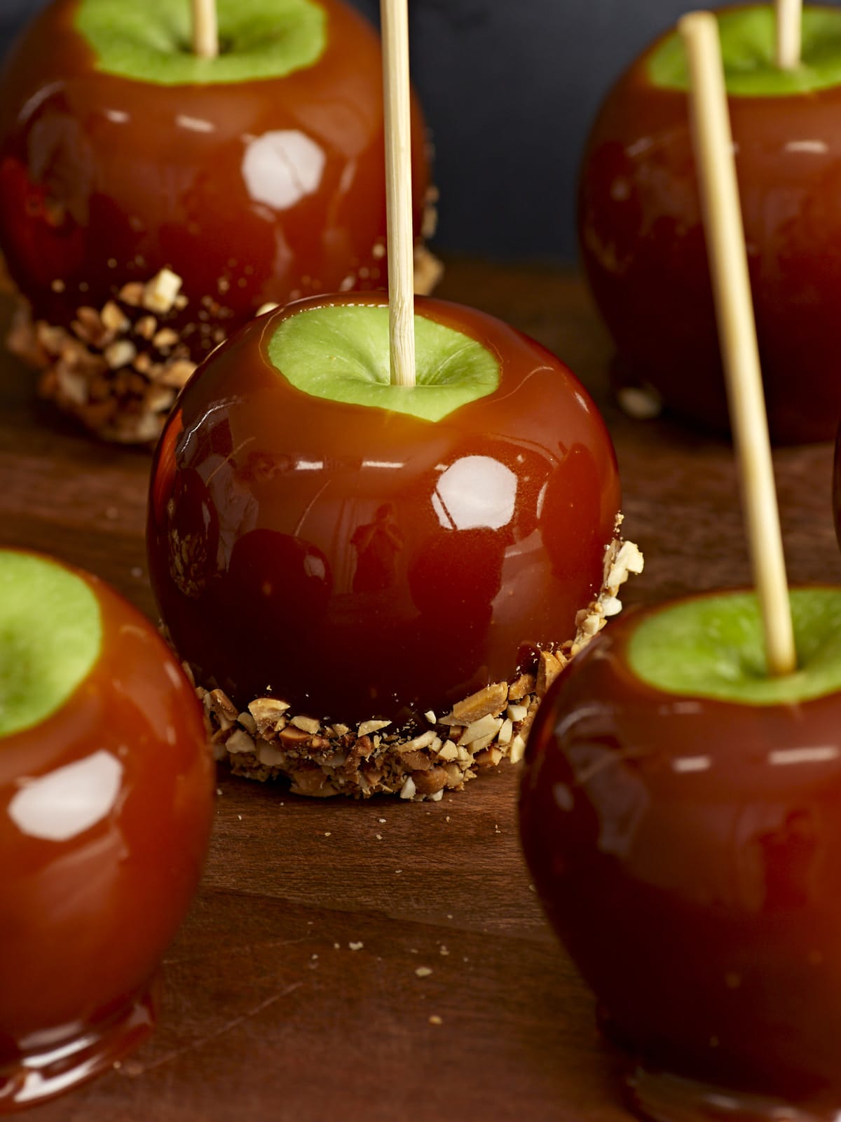 Close up side view of caramel apples on a wooden platter.