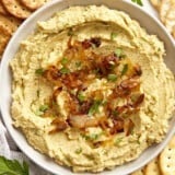 Overhead view of a bowl full of chickpea spread with caramelized onions surrounded by crackers.