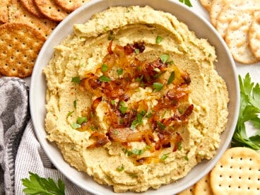 Overhead view of a bowl full of chickpea spread with caramelized onions surrounded by crackers.