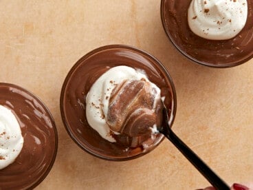 Overhead view of whipped cream being stirred into a cup of pudding.