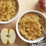 Two small bowls of homemade applesauce with apples and cinnamon on the side.