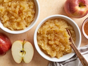 Two small bowls of homemade applesauce with apples and cinnamon on the side.