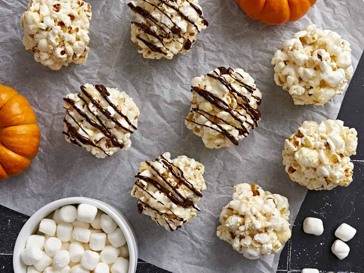 Overhead view of popcorn balls spread out on parchment paper with chocolate drizzled over 4 popcorn balls.