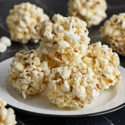 Close up side view of popcorn balls stacked on top of a plate.