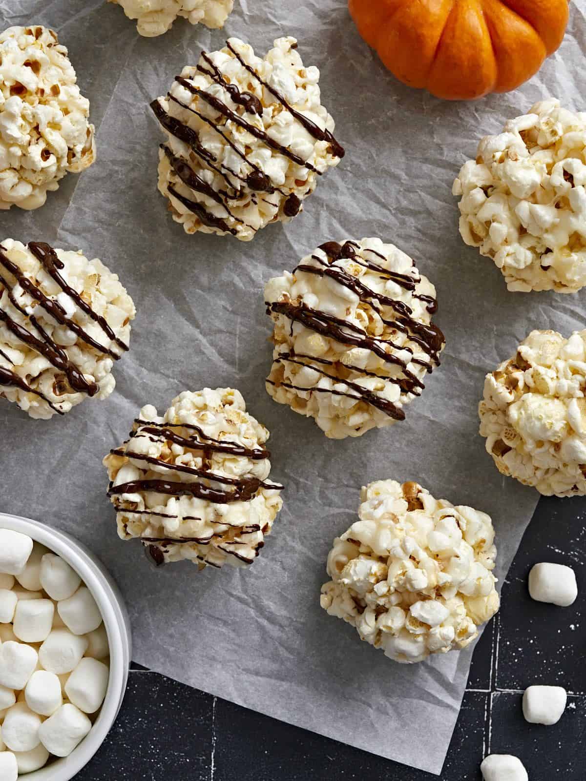 Overhead view of popcorn balls spread out on parchment paper with chocolate drizzled over 4 popcorn balls.