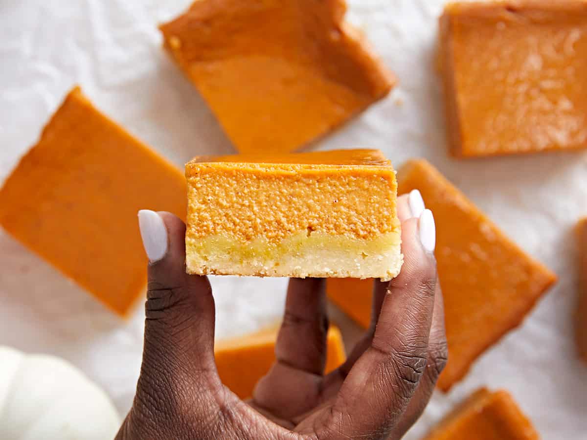 Overhead view of a pumpkin pie bar being held up to the camera on it's cut side.