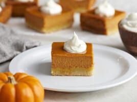 Side view of a pumpkin pie bar on a white plate with whipped cream on top.