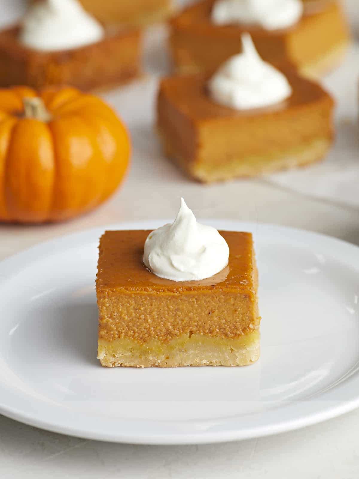 Side view of a pumpkin pie bar on a white plate with whipped cream on top.