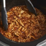 Close up side view of salsa chicken in the crock pot with tongs.