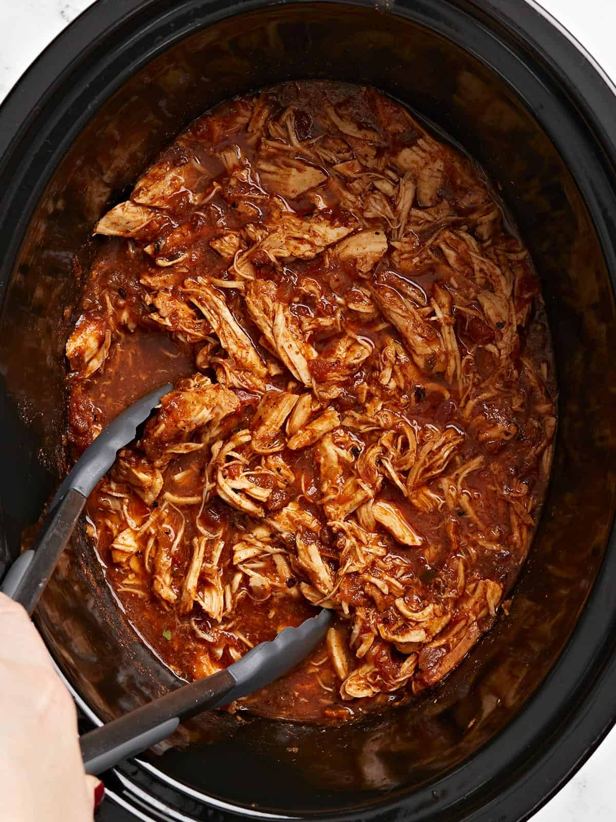 Close up overhead view of salsa chicken in the crock pot with tongs.