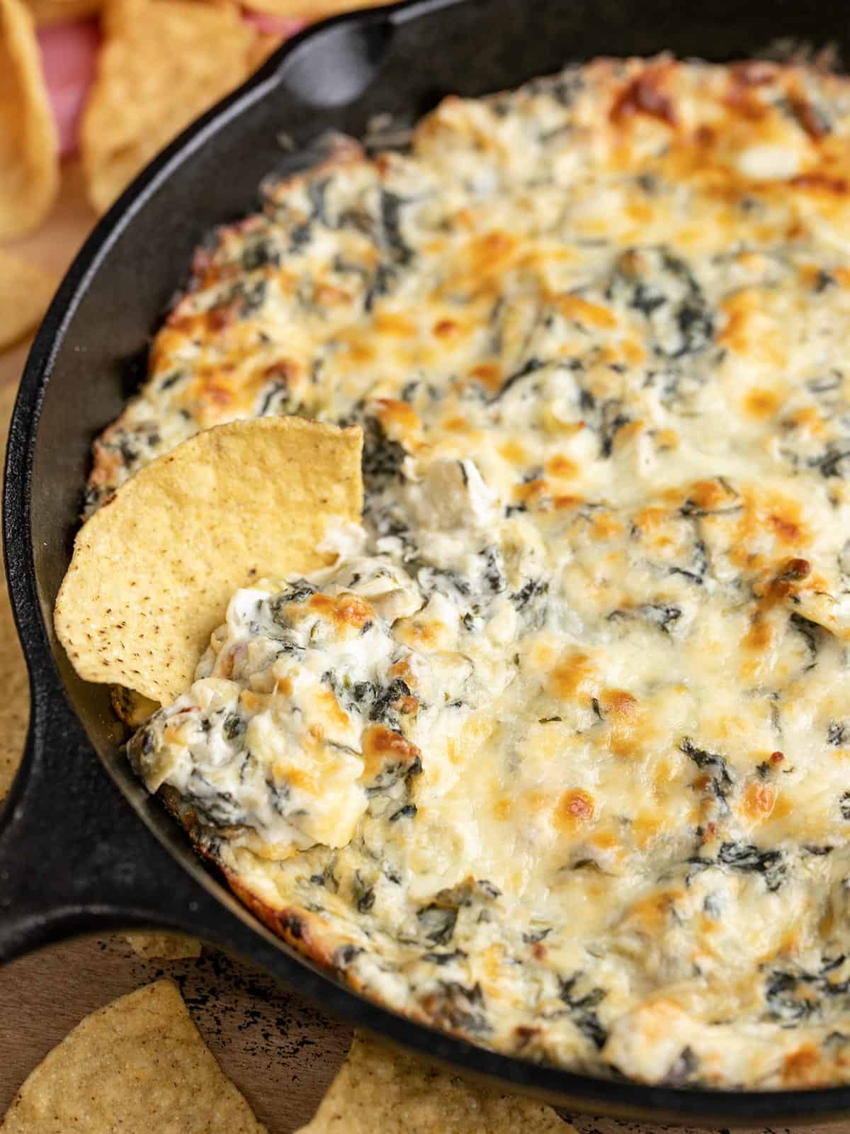 Close up side view of a skillet full of spinach artichoke dip with a tortilla chip.