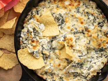 Close up overhead view of a skillet full of spinach artichoke dip with tortilla chips dipped into it.