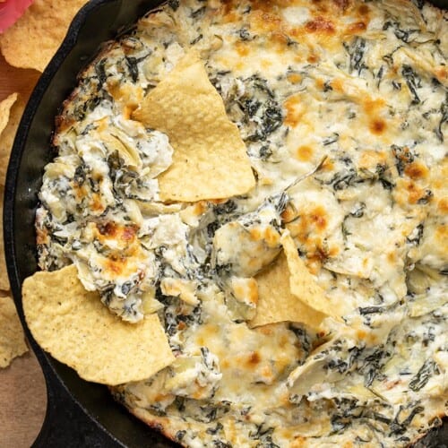 Close up overhead view of a skillet full of spinach artichoke dip with tortilla chips dipped into it.