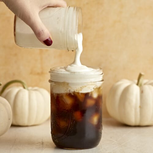 Sweet Cream Cold Foam being poured over a jar full of iced coffee.