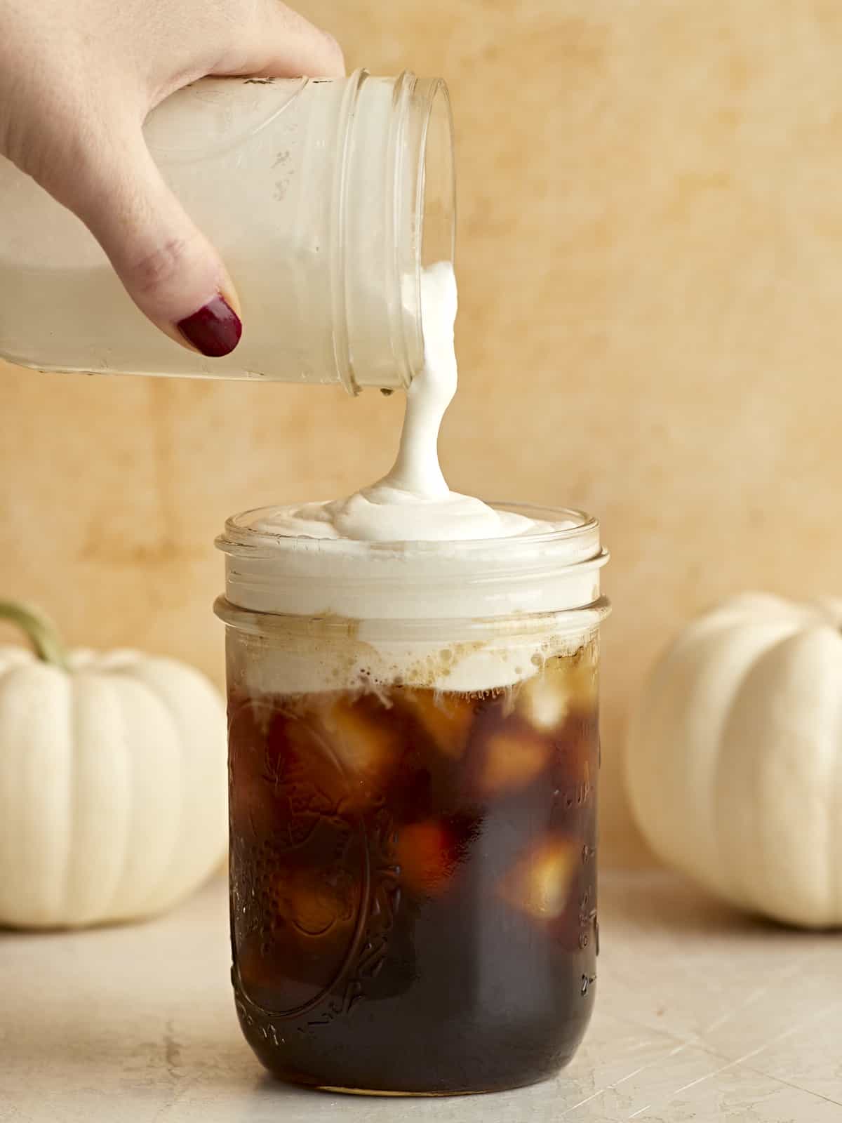 Sweet cream cold foam being poured over a mason jar full of iced coffee.