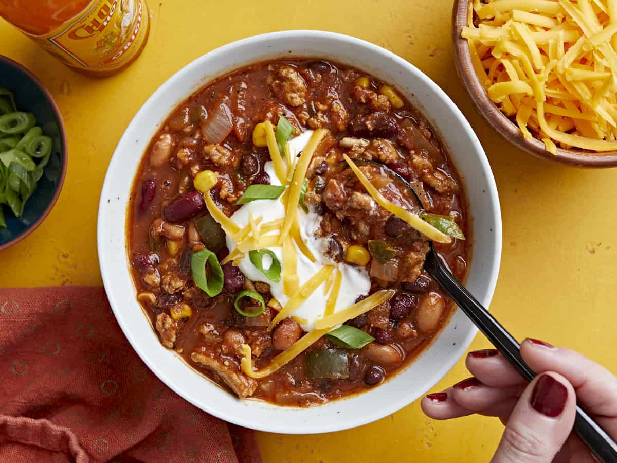Overhead view of a bowl full of chili with toppings and a spoon dipping into the center.
