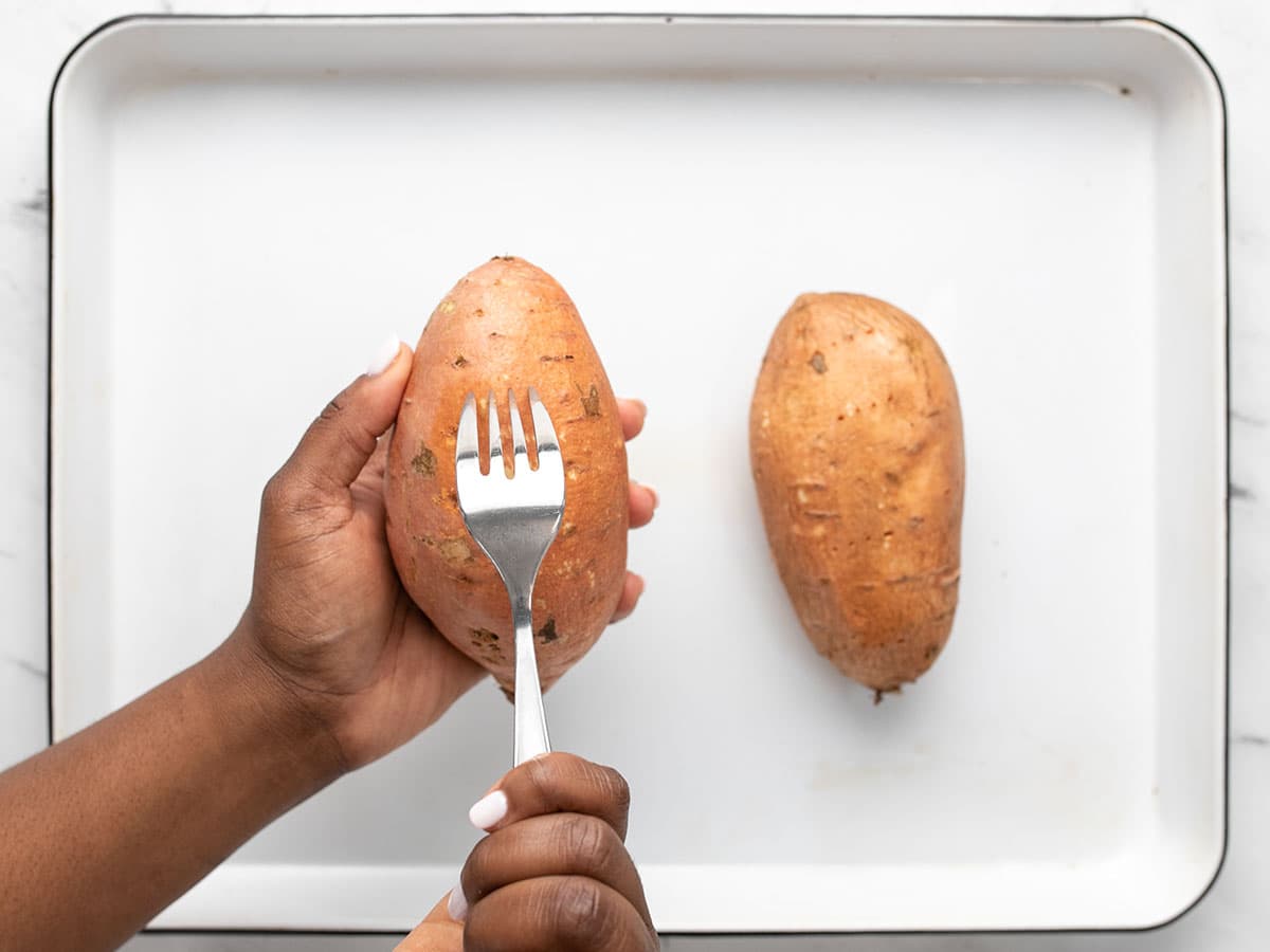 Overhead view of sweet potatoes being pricked with a fork.