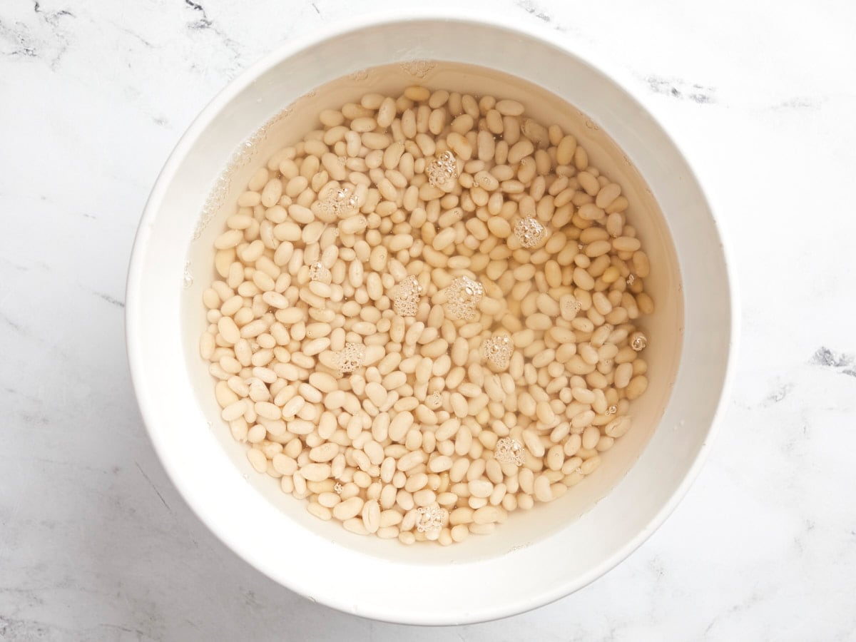 Overhead view of Navy Beans being soaked in water in a bowl.