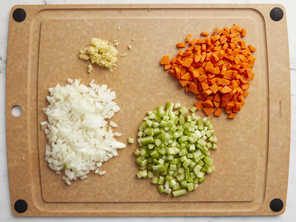 Diced carrots, diced onion, diced celery, and minced garlic on a cutting board.