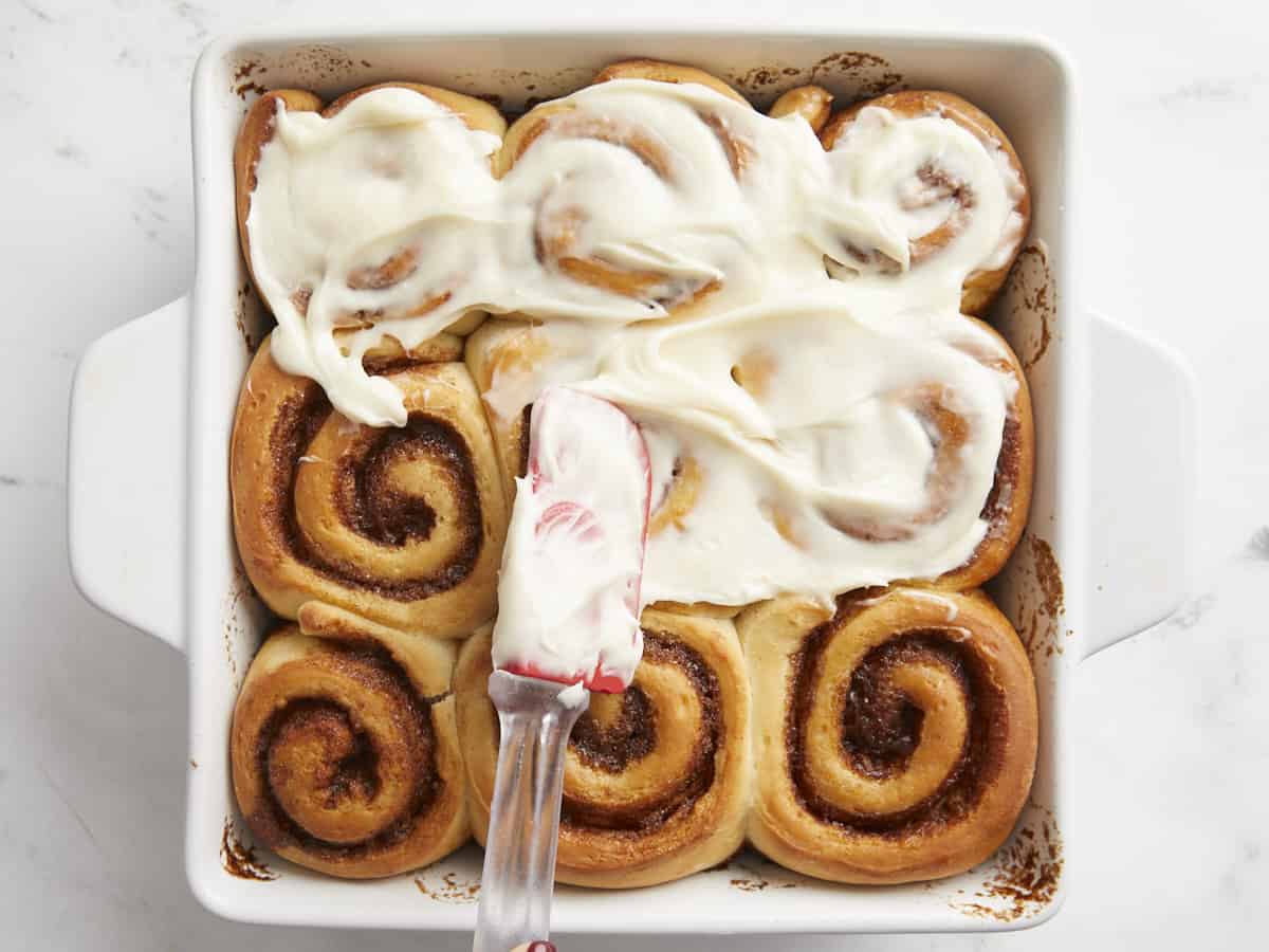Cream cheese frosting being spread onto the cinnamon rolls. 
