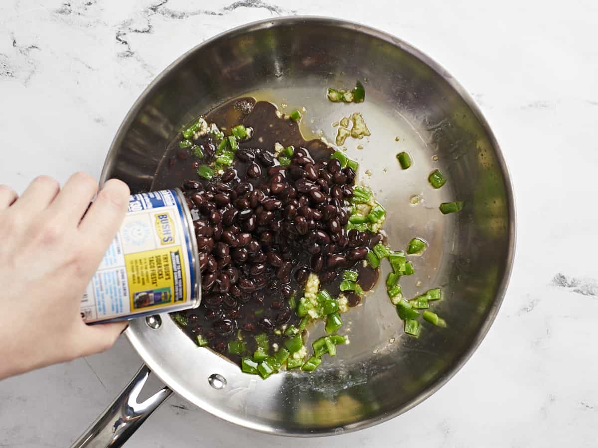 Black beans being poured into the skillet. 