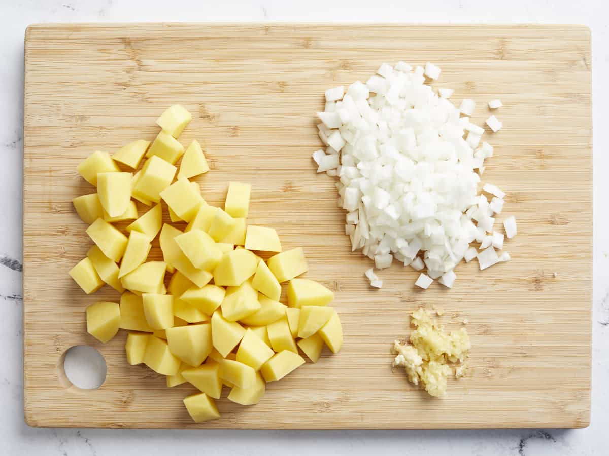 Overhead view of diced onion, potatoes and garlic on a cutting board.