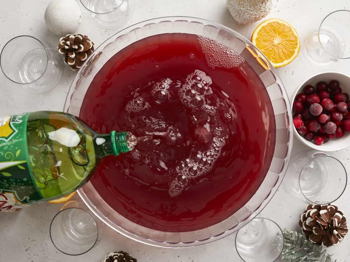 Ginger ale being poured into a punch bowl with cranberry juice and apple cider.
