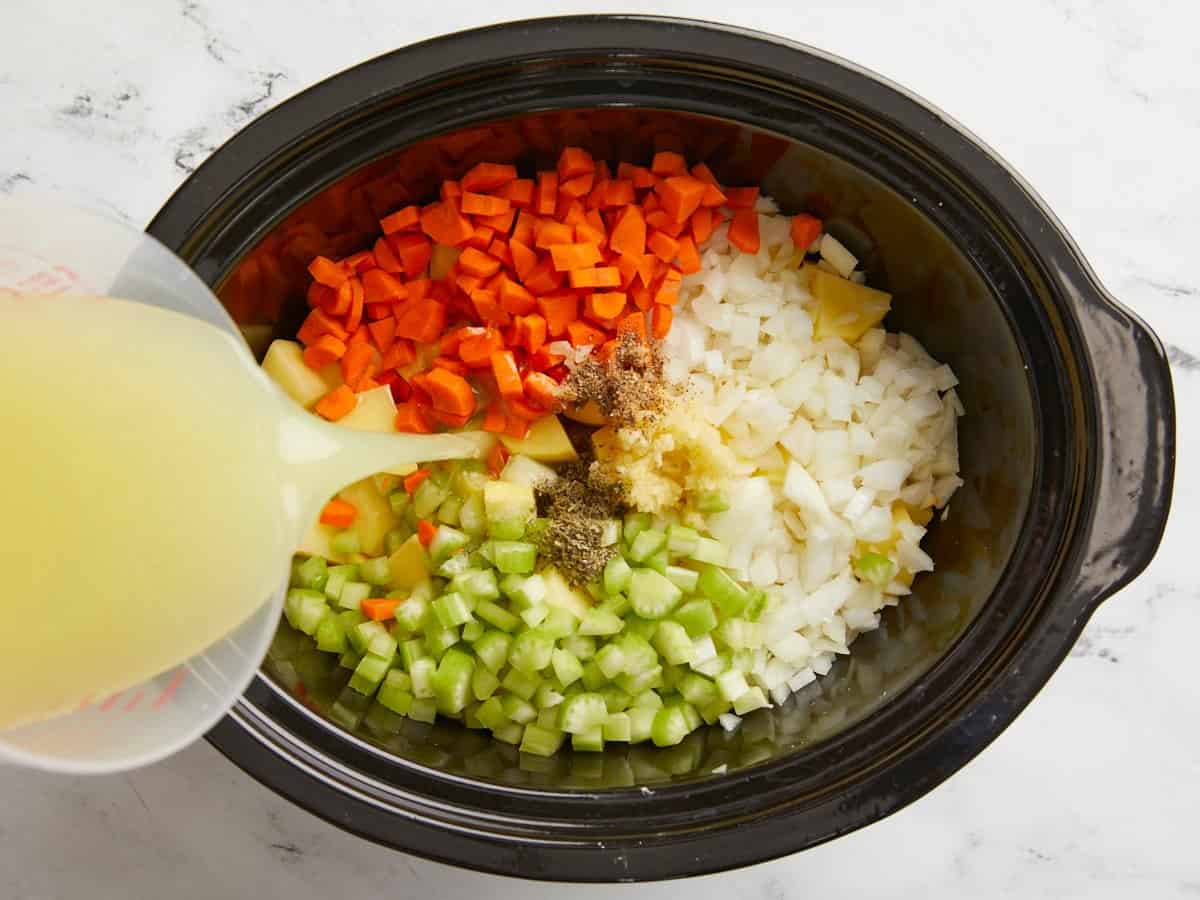 Diced vegetables, potatoes, seasoning and chicken broth added to a slow cooker.