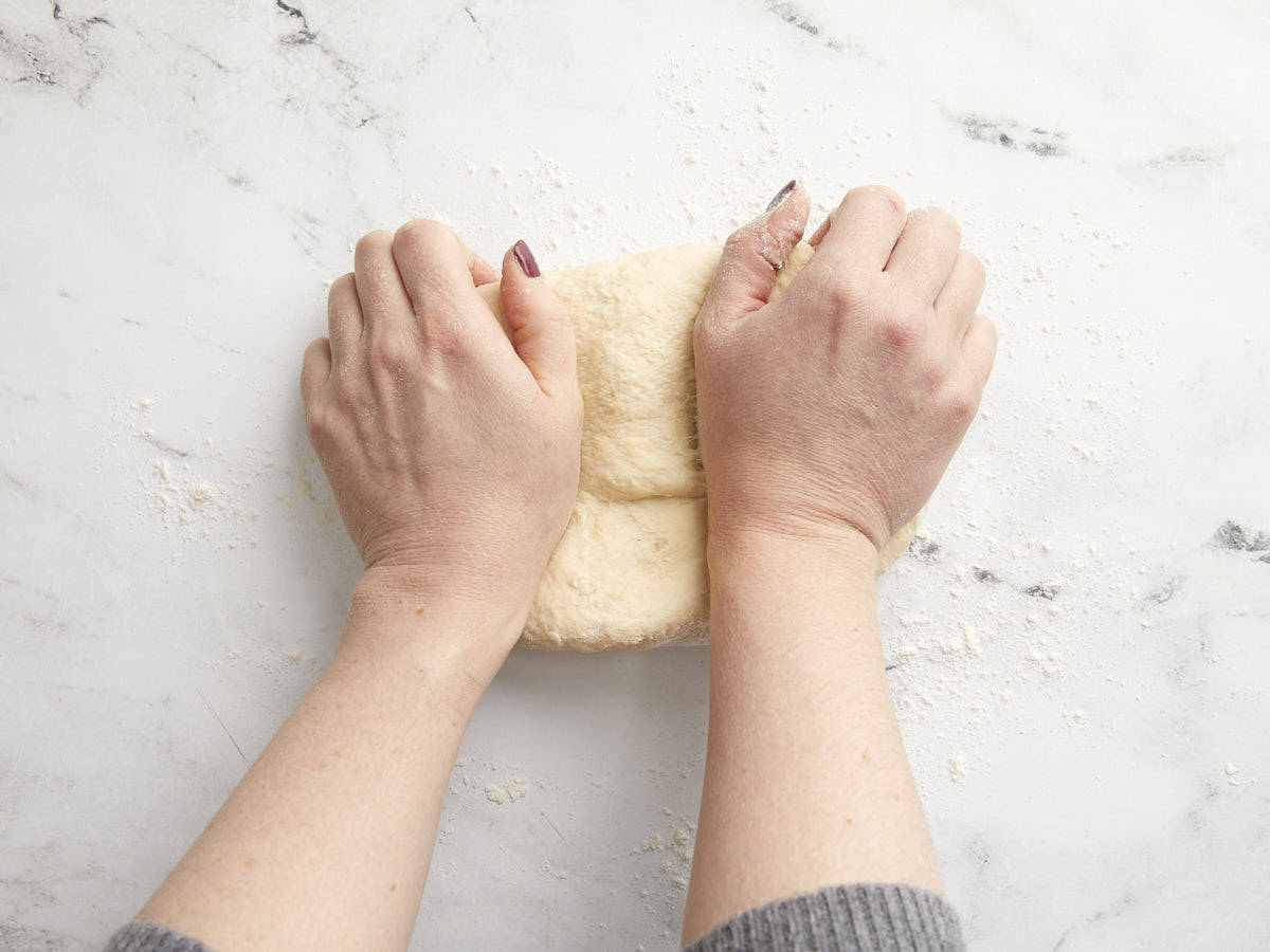Dough being kneaded by hand on a marble surface.