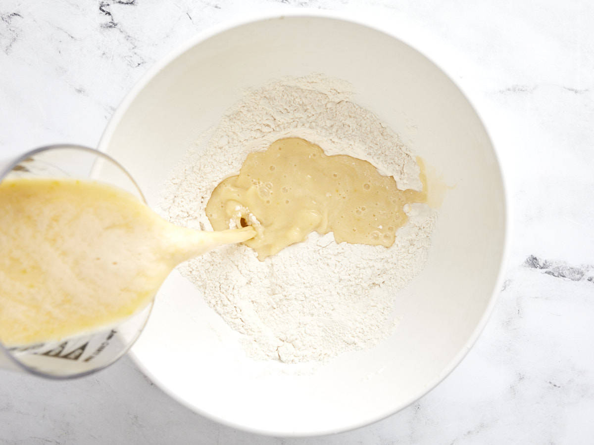 Liquid ingredients being poured into a bowl with flour and salt.