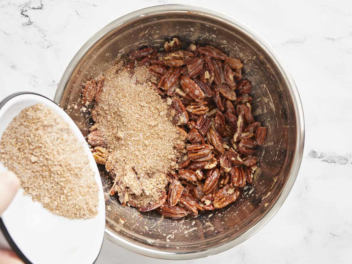 Pecans in the bowl coated in egg white, cinnamon sugar being poured over top. 