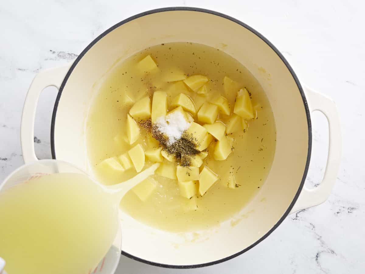 Overhead view of potatoes, spices, and chicken broth being added to the pot.