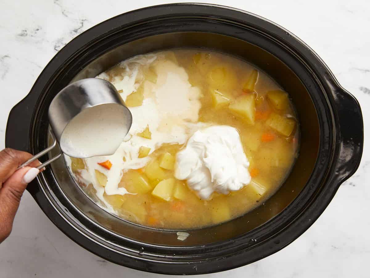 Heavy cream and sour cream added to potato soup in a slow cooker.