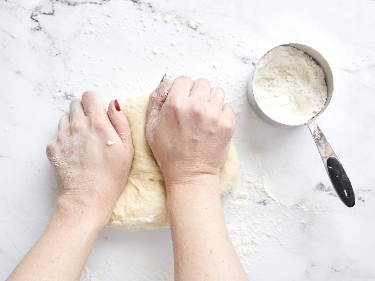 Kneading dough with flour in a measuring cup on the side.