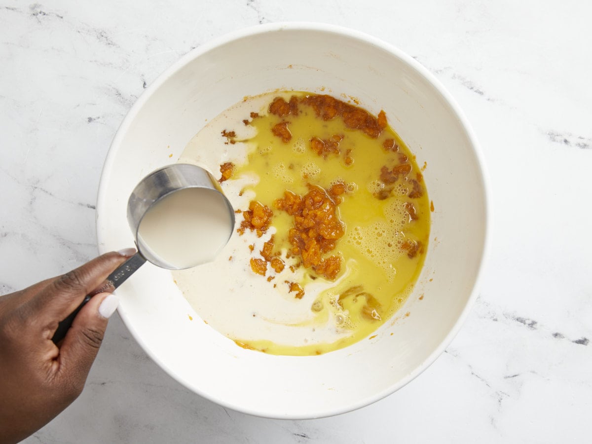 Evaporated milk and eggs being added to mashed sweet potato mixture.