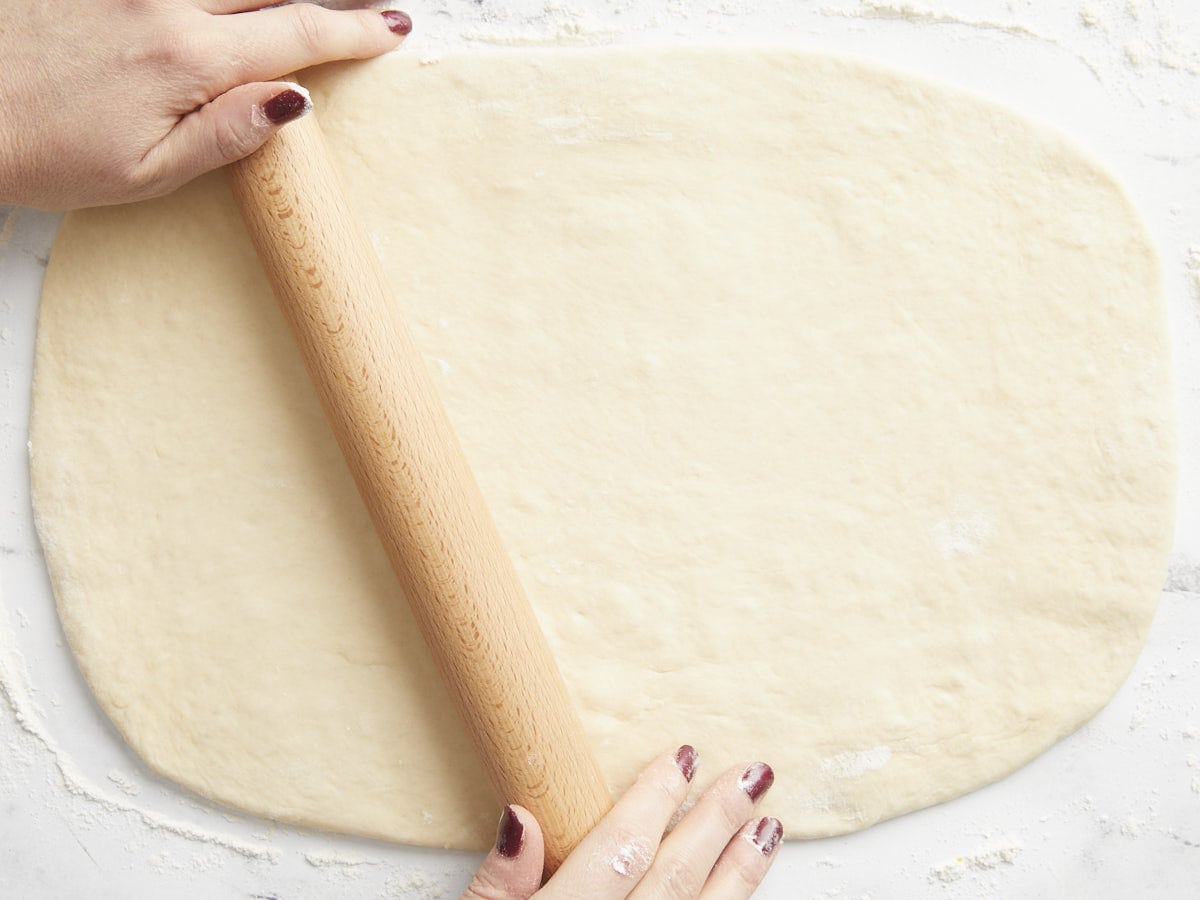 Cinnamon roll dough being rolled out into a rectangle. 