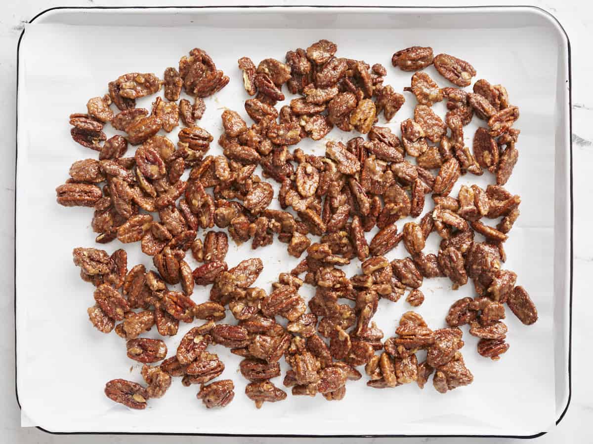 Candied pecans spread onto a baking sheet, ready to bake. 