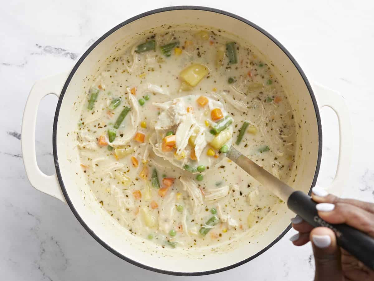 Overhead view of finished chicken pot pie soup in the dutch oven pot with ladle scooping some out.