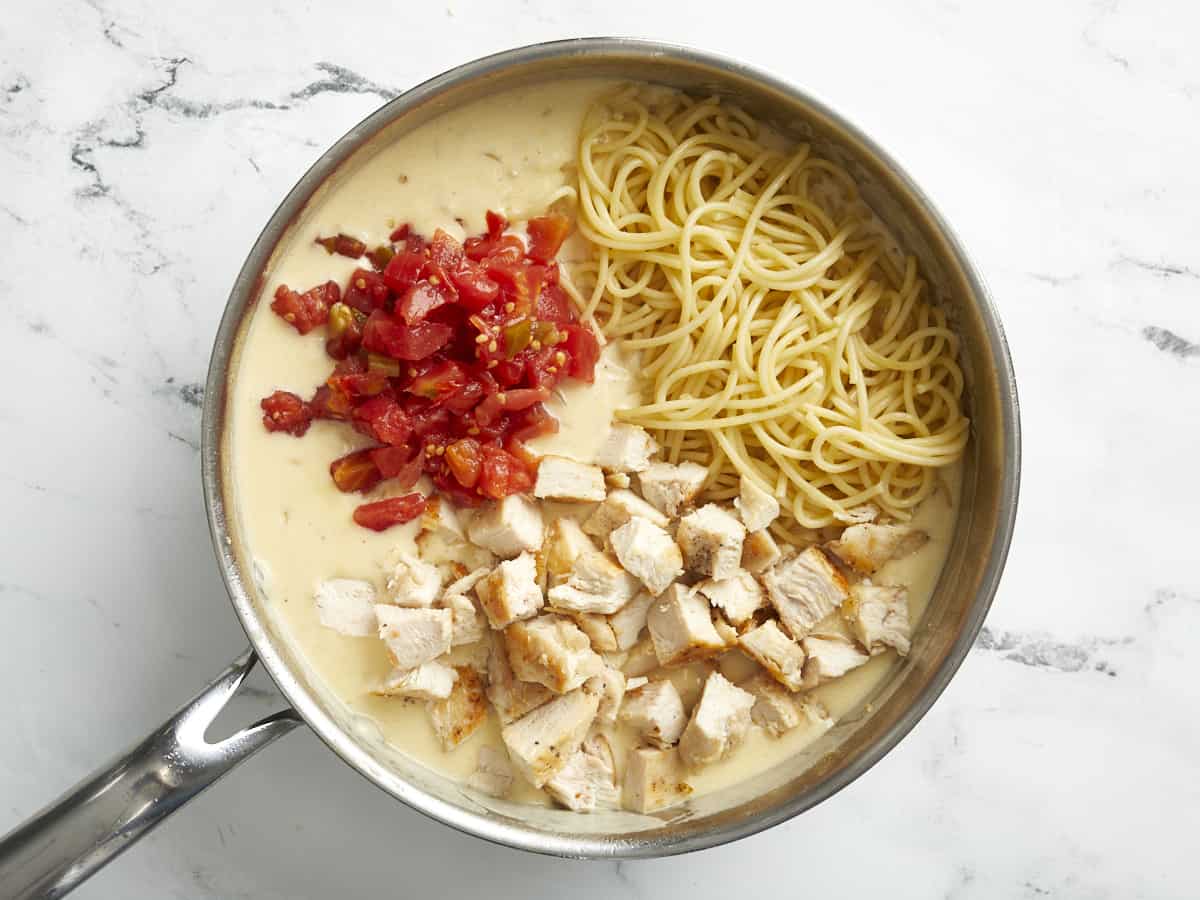 Cooked spaghetti, chopped chicken breasts, and rotel being added to skillet.