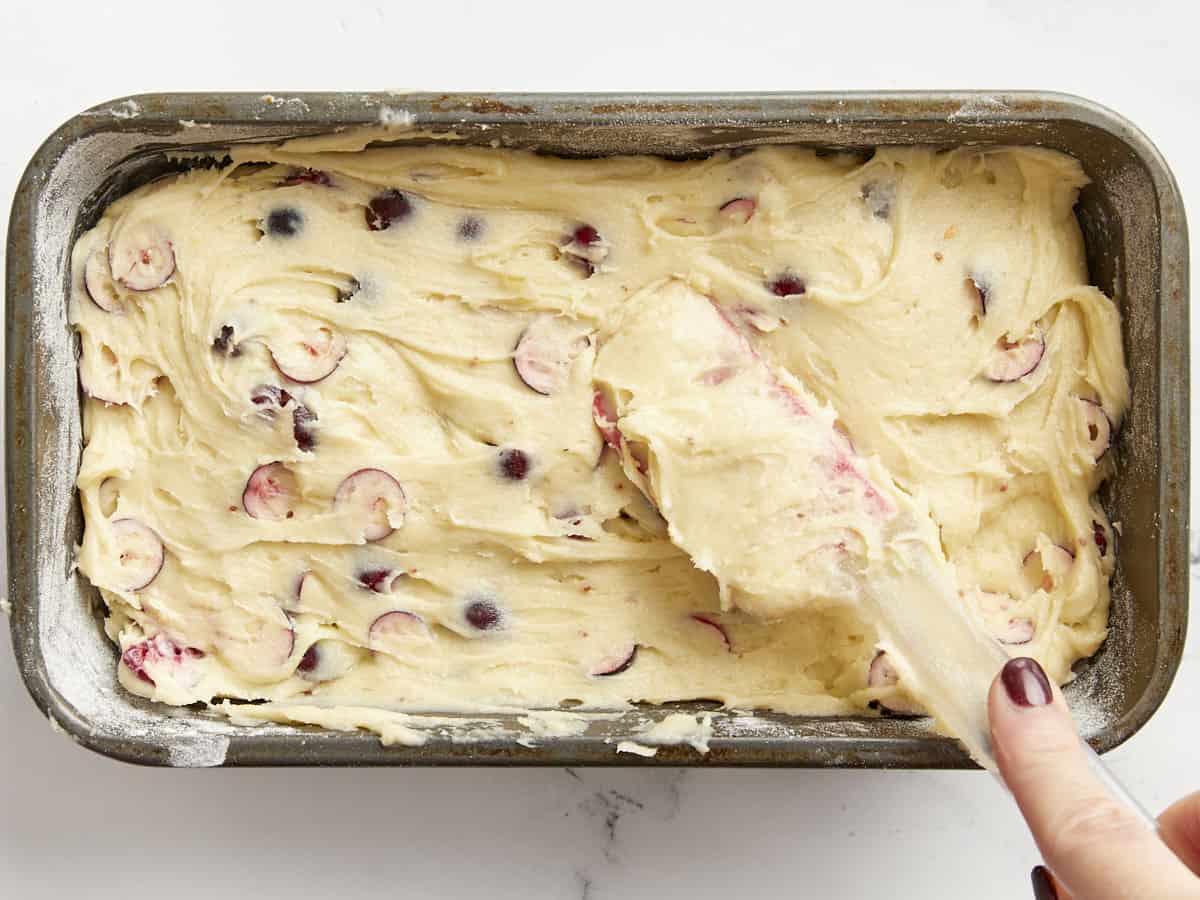 Cranberry bread batter being smoothed into a bread pan. 