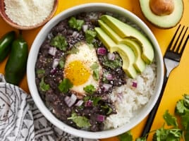 Overhead view of a bowl of black beans with eggs over rice with sliced avocado on the side.