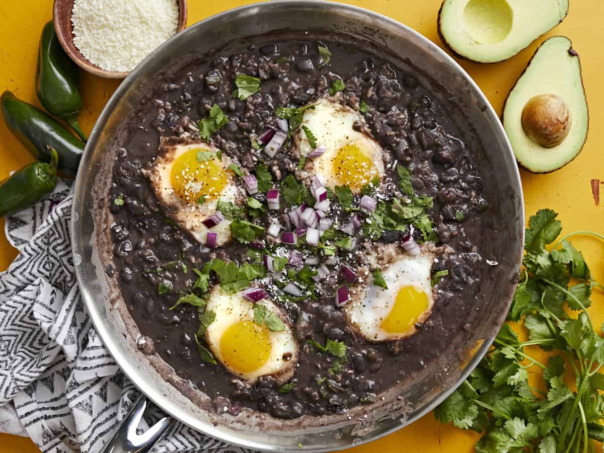 Overhead view of eggs poached in a skillet full of black beans garnished with cilantro and red onion.