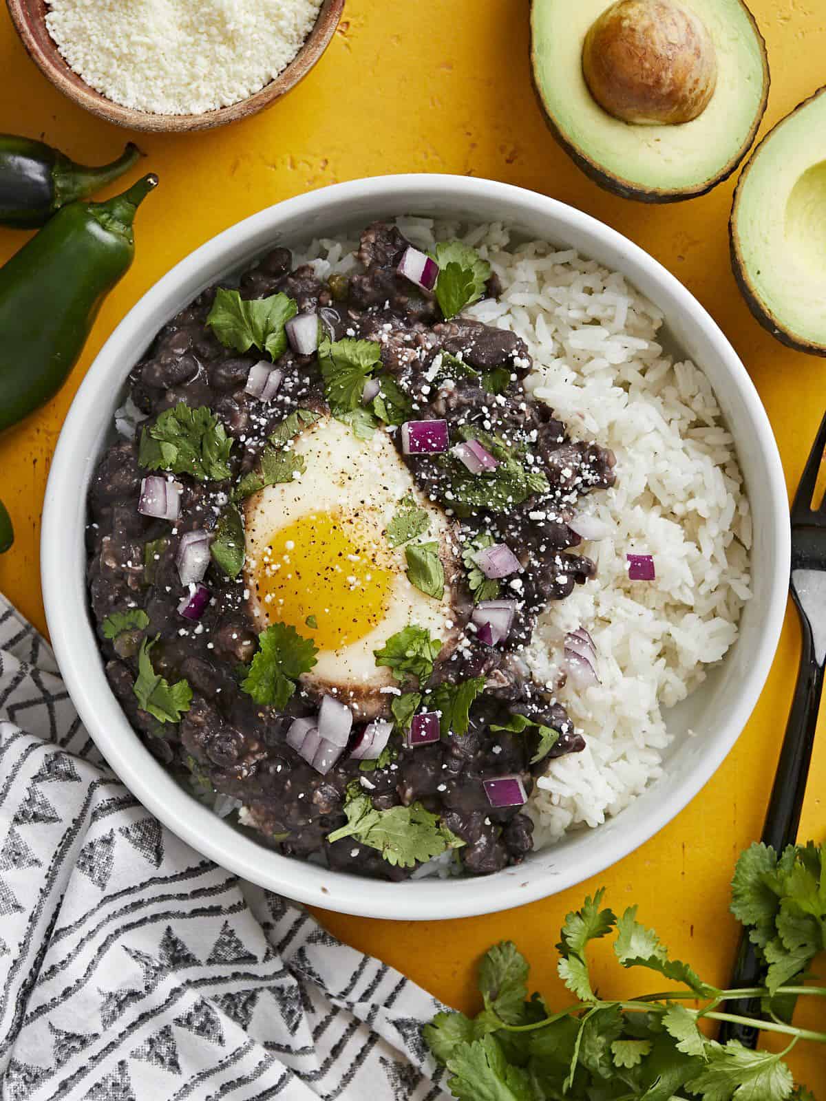 Overhead view of a bowl full of rice, black beans and eggs garnished with onion and cilantro.