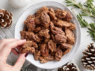 Overhead view of a bowl full of candied pecans and a hand grabbing a few.