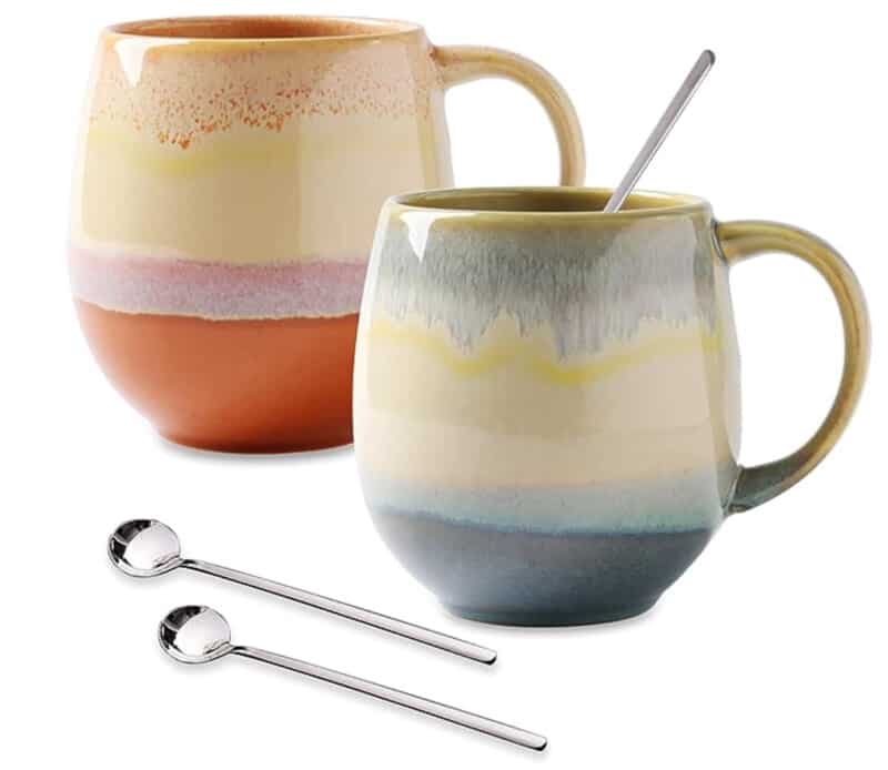 Two ceramic mugs with colorful glaze and metal spoons. 