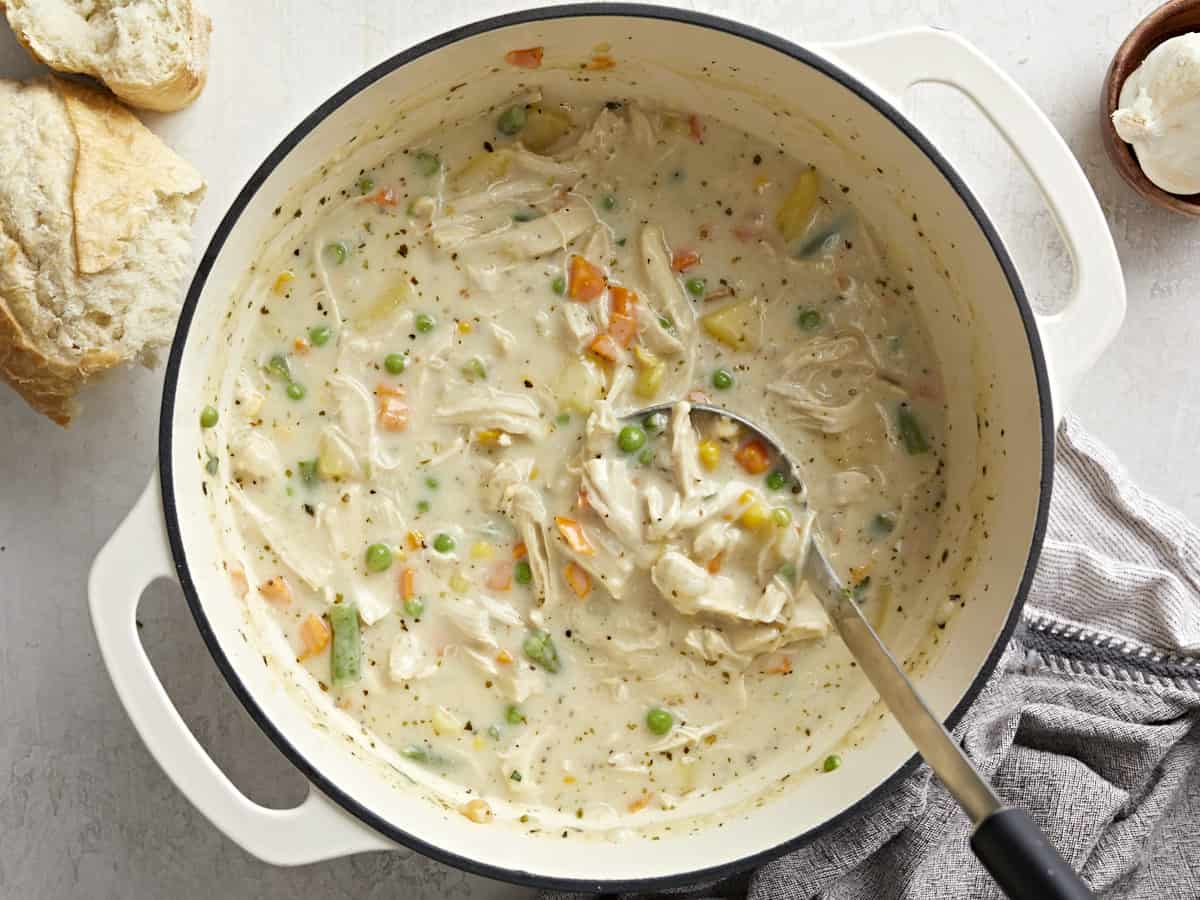 Overhead view of a pot full of chicken pot pie soup with a ladle scooping some out.