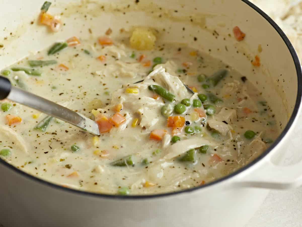Side view of chicken pot pie soup in a large pot with a ladle scooping some out.