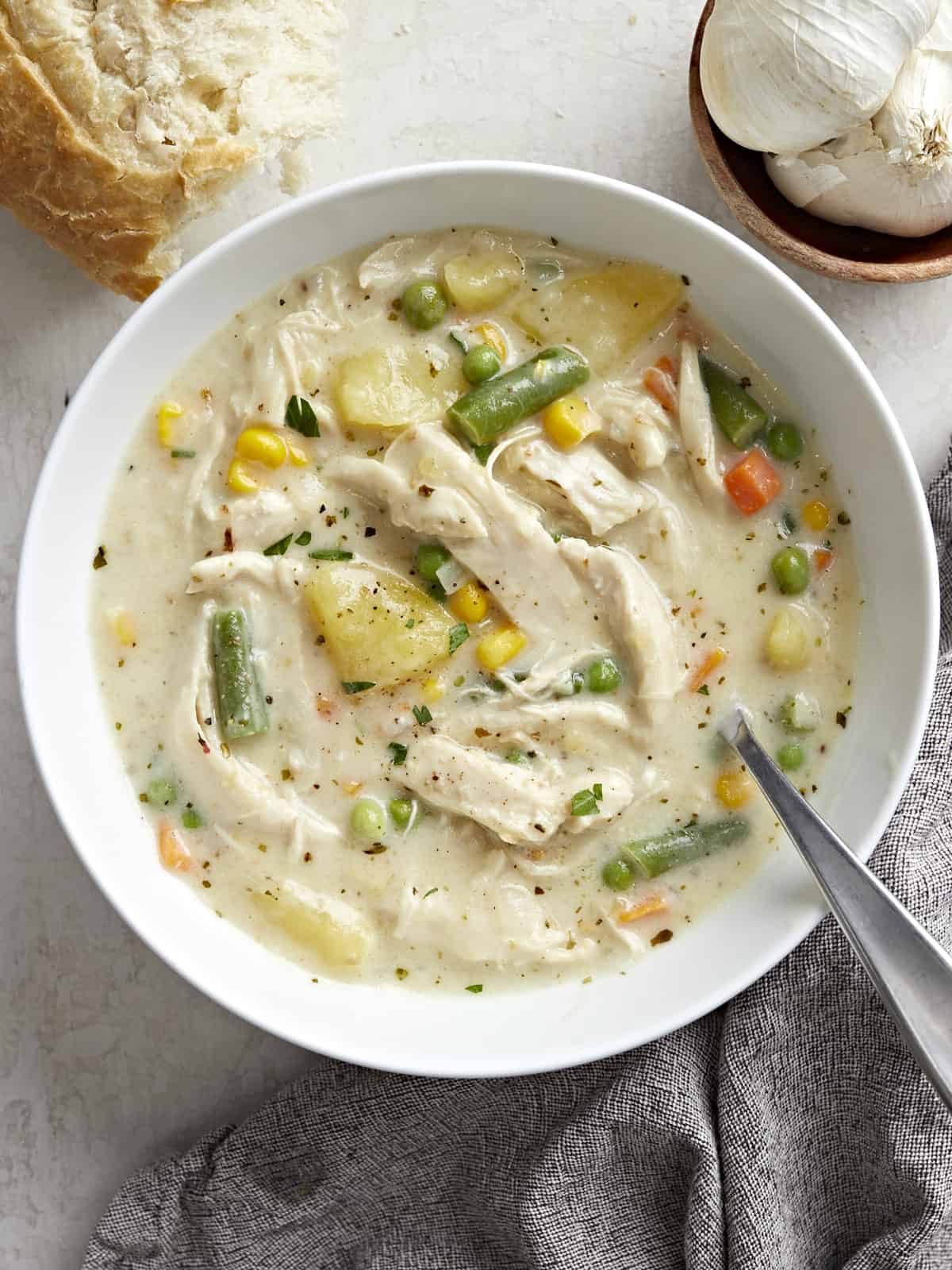 Overhead view of a bowl of chicken pot pie soup with crusty bread on the side and a spoon inside the bowl.