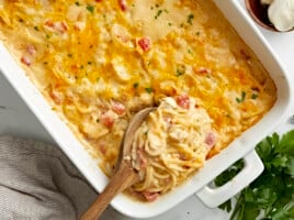 Overhead view of chicken spaghetti in a white casserole dish with a wooden spoon placed inside.